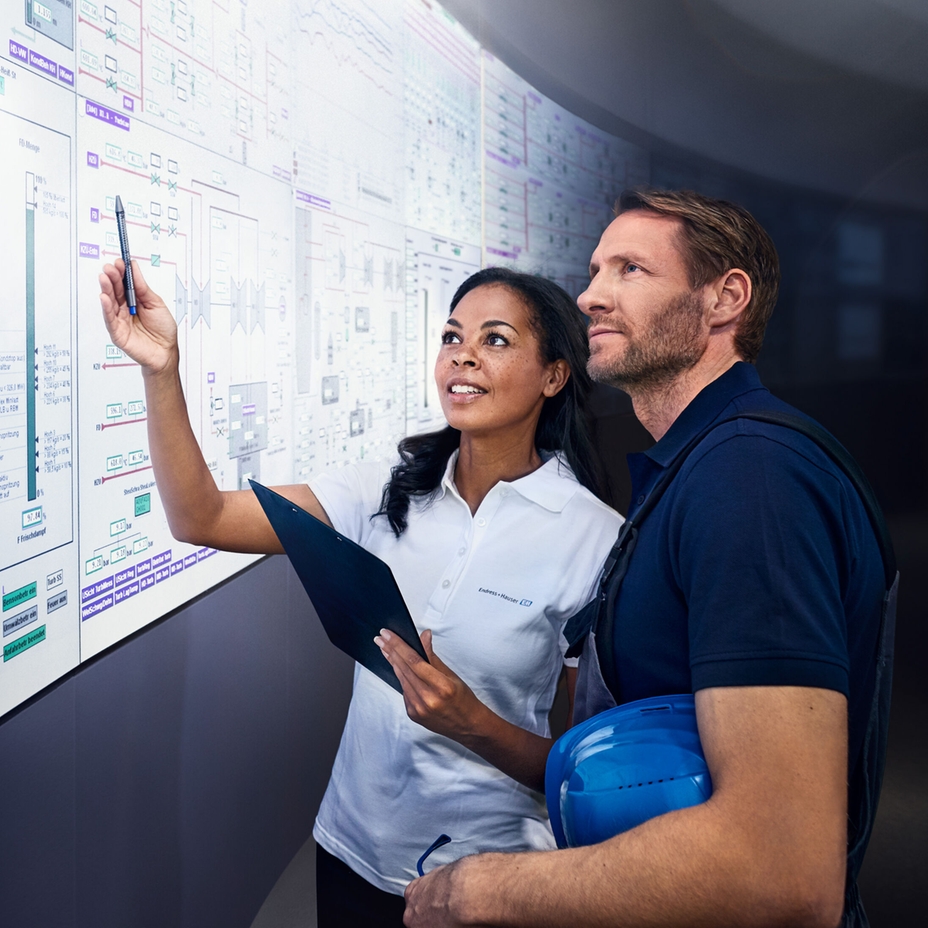 Dos ingenieros miran una gran pantalla en una sala de control industrial.