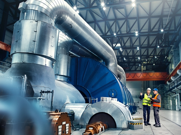 Dos ingenieros conversan junto a una turbina de generación de energía.